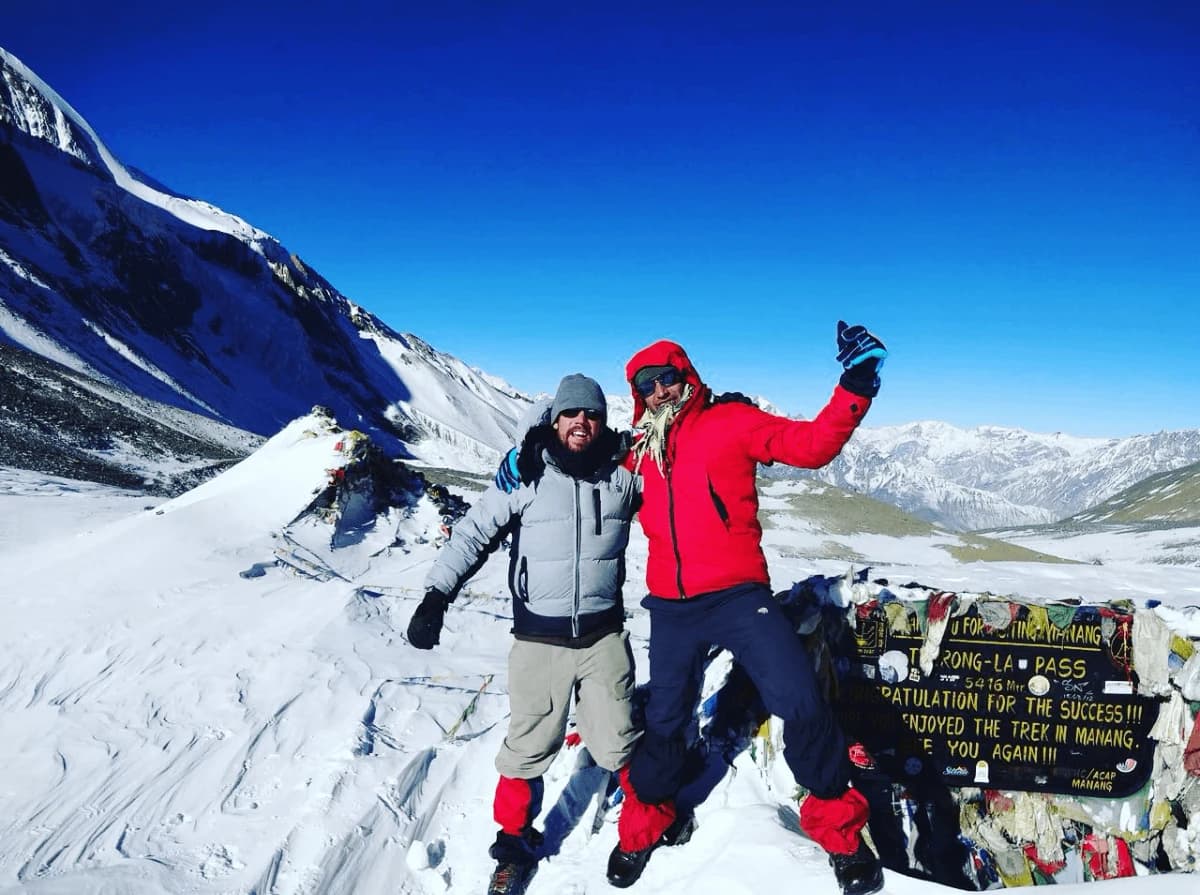 Trekkers and their guide celebrating at Thorong La Pass (5,416m) during the Manaslu Annapurna Circuit Trek in Nepal.